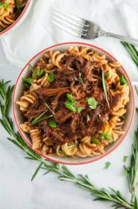 Crock Pot beef ragu in a bowl with noodles and sprigs of rosemary