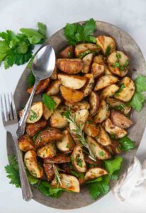 Garlic and Herb Roasted Red Potatoes make a delicious side dish. Shown on a silver serving plate with greens.