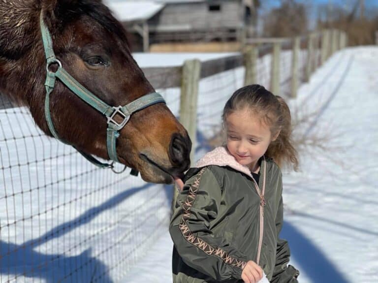 Horse licking a girl's hood in the snow