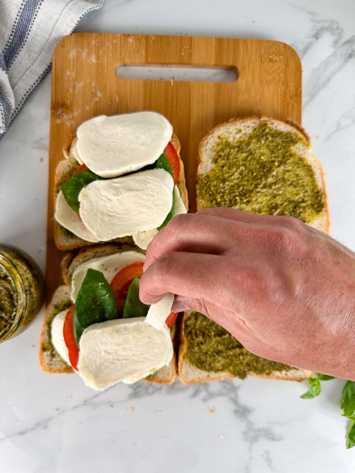 Build the caprese panini sandwich with pesto by layering mozzarella, tomatoes, and basil on sliced of bread slathered with pesto.