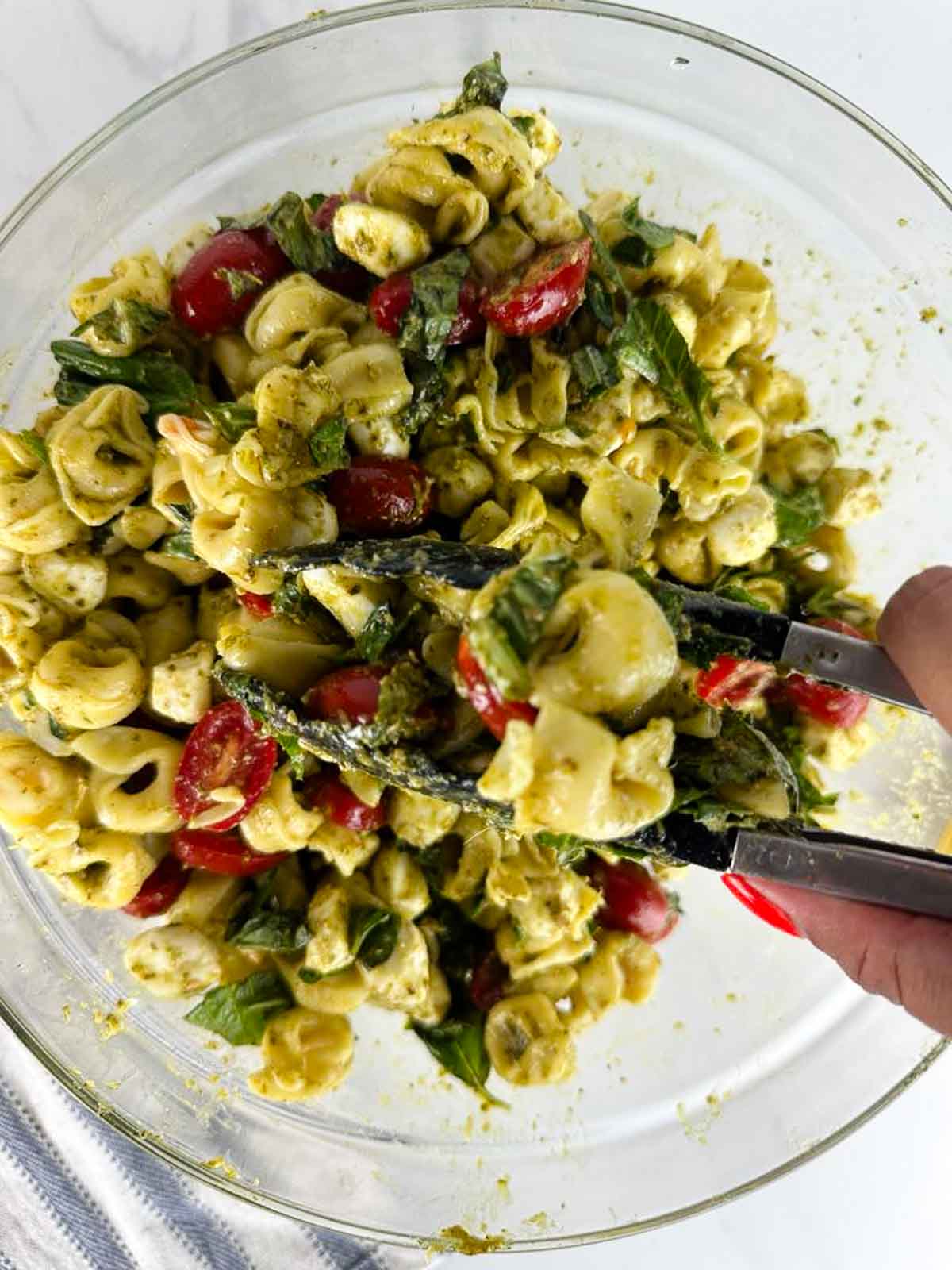 Toss the caprese tortellini pasta salad with pesto to evenly coat everything.
