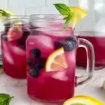 a photo of 2 glasses of blueberry vodka lemonade cocktails garnished with lemon wedges, blueberries, and mint in a text box reading boozy blueberry lemonade