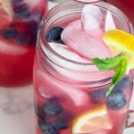 a photo of 2 glasses of blueberry vodka lemonade cocktails garnished with lemon wedges, blueberries, and mint in a text box reading blueberry vodka lemonade