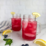 Two mason jar mugs of blueberry lemonade