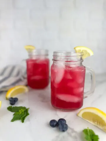 Two mason jar mugs of blueberry lemonade