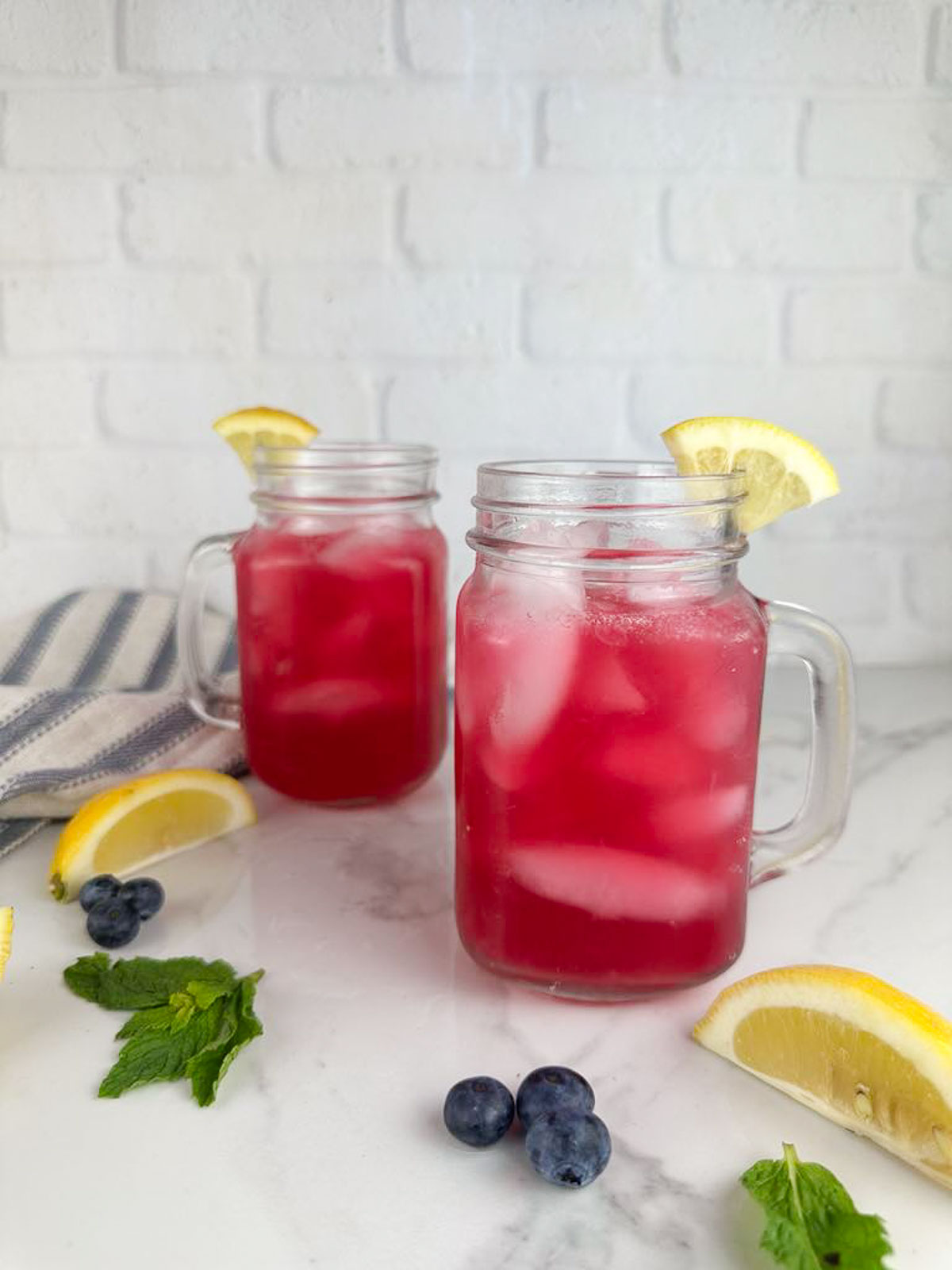 Two mason jar mugs of blueberry lemonade