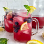 2 glasses of blueberry vodka lemonade cocktails garnished with lemon wedges, blueberries, and mint