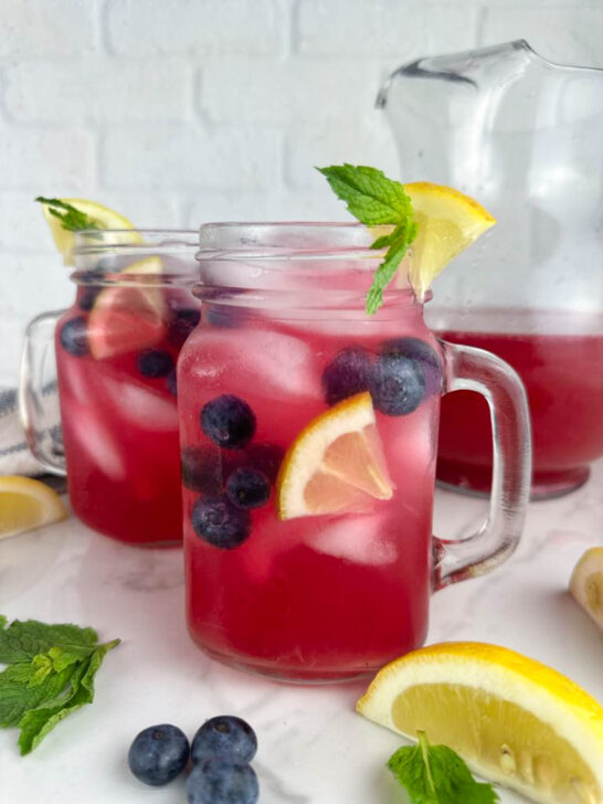 2 glasses of blueberry vodka lemonade cocktails garnished with lemon wedges, blueberries, and mint