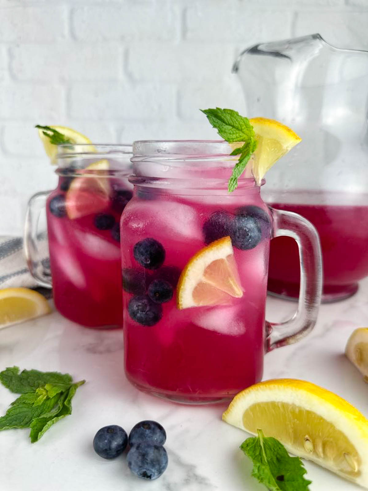 2 glasses of blueberry vodka lemonade cocktails garnished with lemon wedges, blueberries, and mint