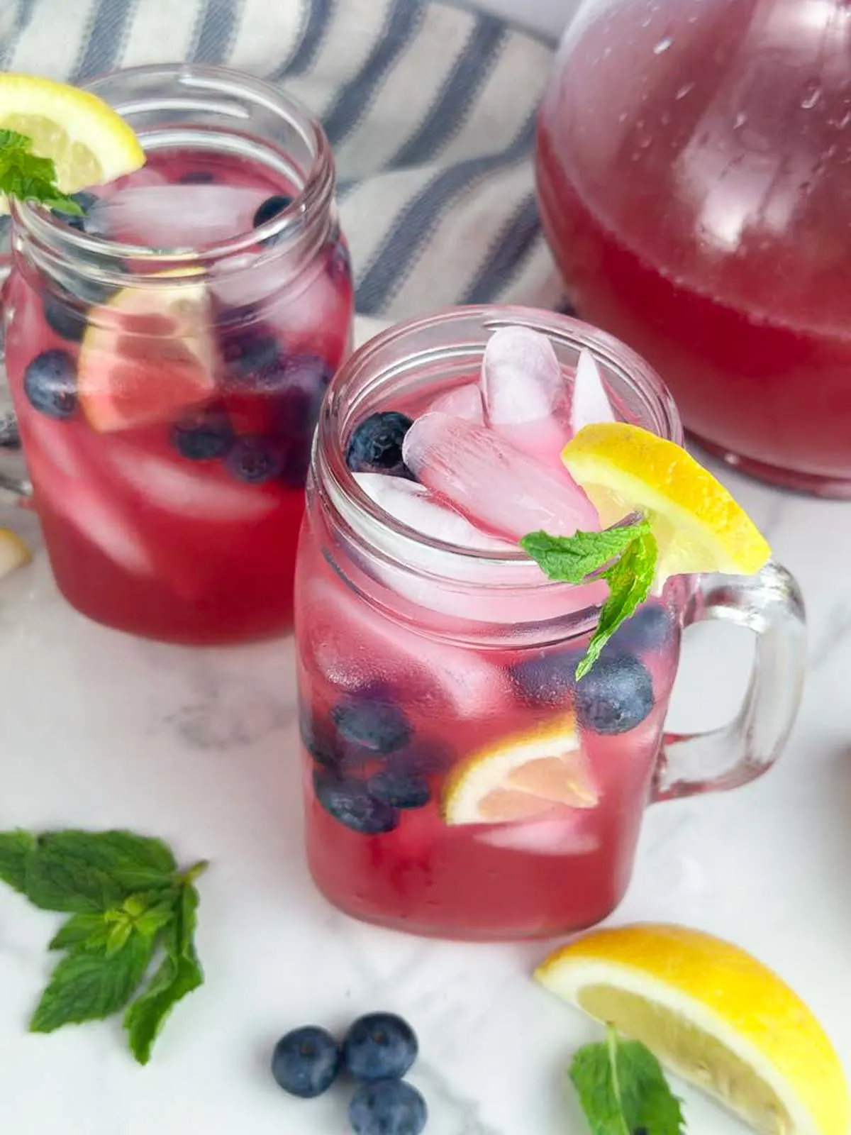 2 glasses of blueberry vodka lemonade cocktails garnished with lemon wedges, blueberries, and mint