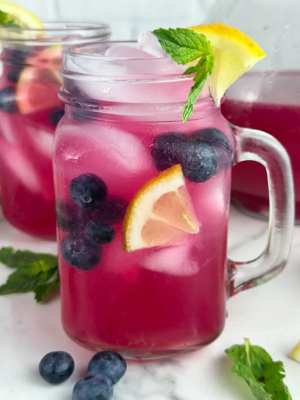 2 glasses of blueberry vodka lemonade cocktails garnished with lemon wedges, blueberries, and mint