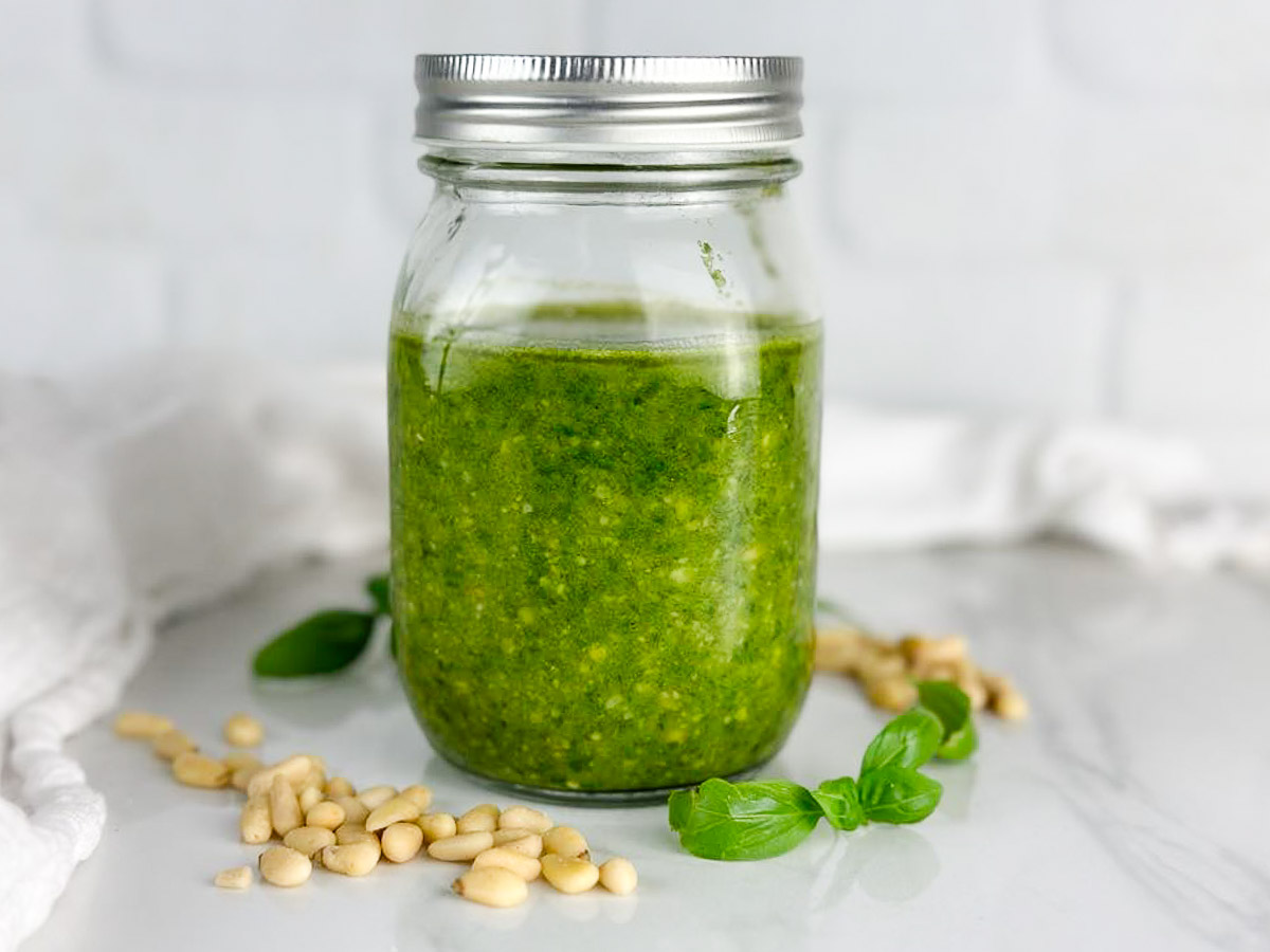 a jar of pesto alla Genovese surrounded by pine nuts and basil