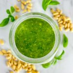 a jar of pesto alla Genovese surrounded by pine nuts and basil