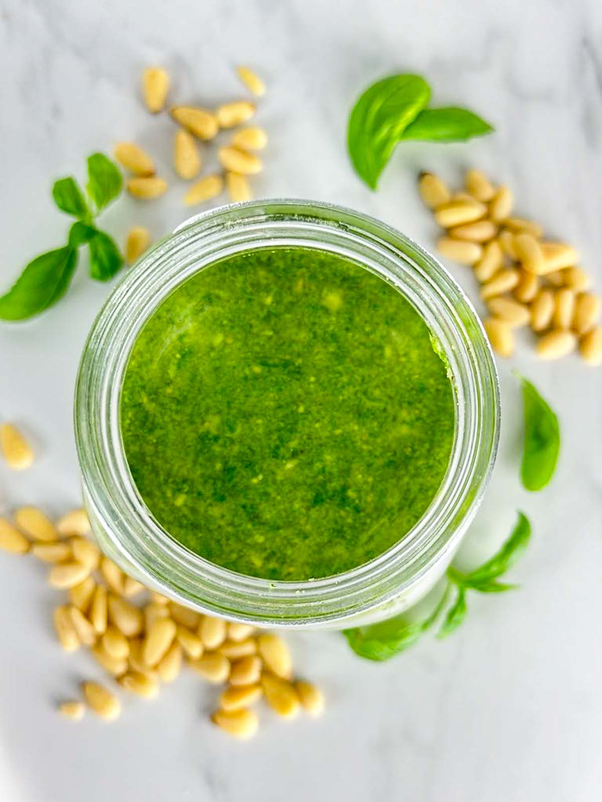 a jar of pesto alla Genovese surrounded by pine nuts and basil