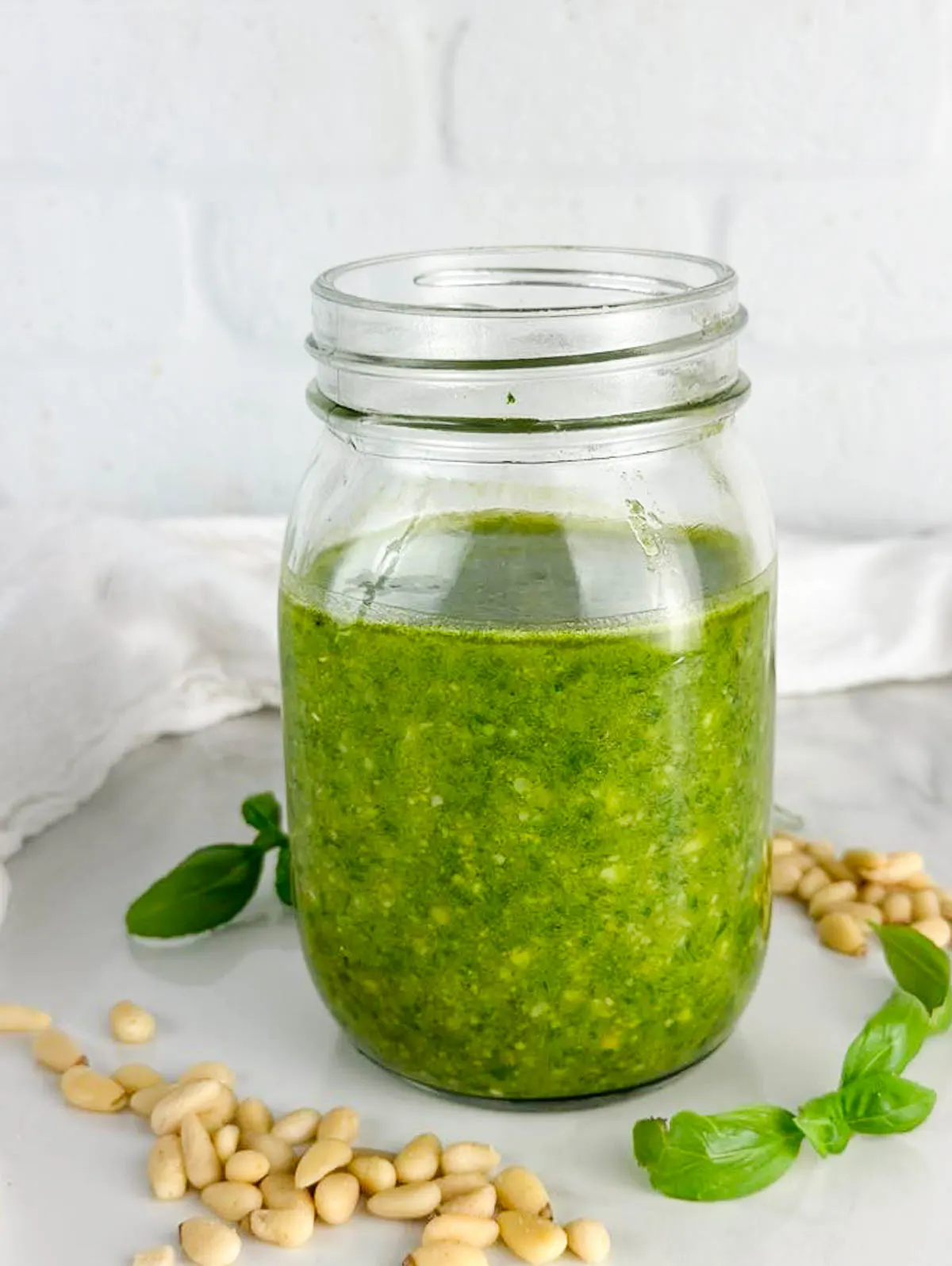 a jar of pesto alla Genovese surrounded by pine nuts and basil