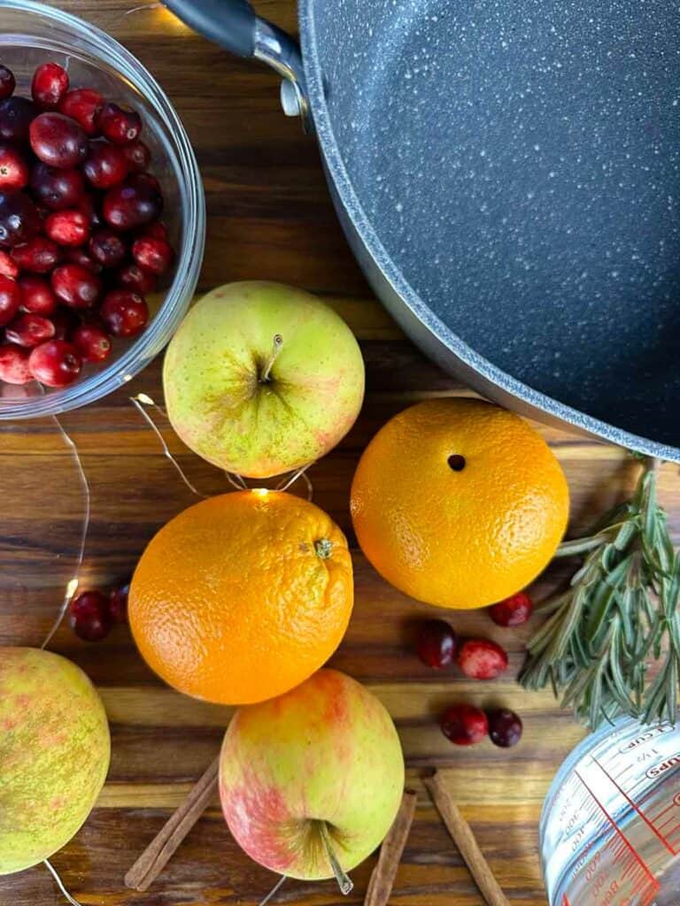 Ingredients for a scented Christmas simmer pot: oranges, cranberries, apples, spice, fresh herbs, and water