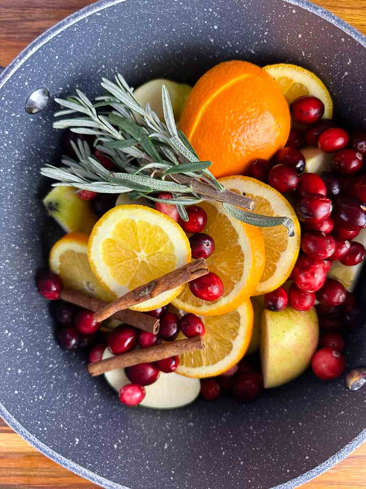 Add the oranges, apples, spices, and herbs to a large pot