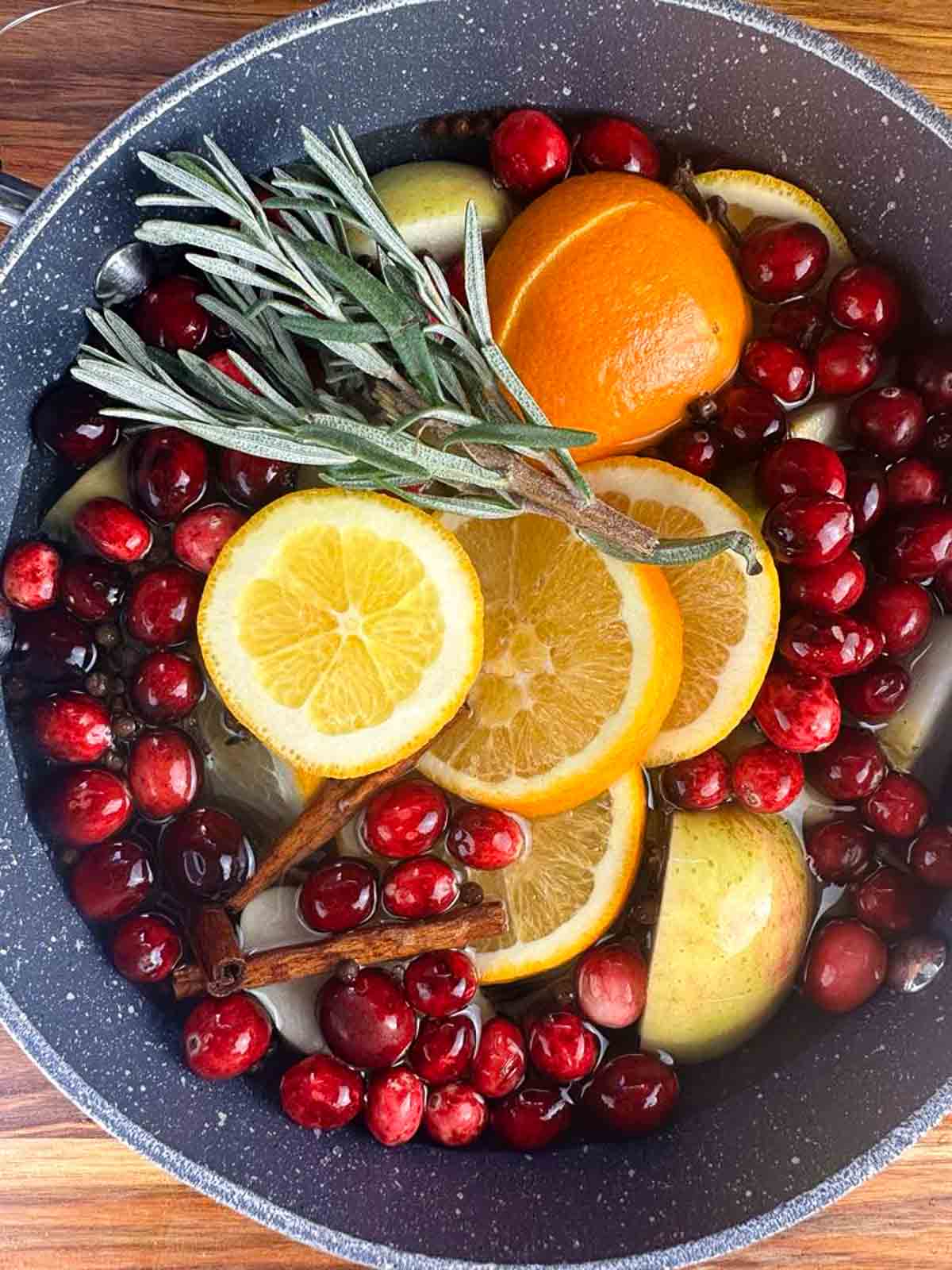 Cover the oranges, apples, spices, and herbs with enough water to cover the apples and make the cranberries float in a large pot