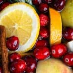 A photo of a blend of cranberries cinnamon sticks, fresh herbs, and oranges in water to make a christmas simmer pot set into a text box reading christmas simmer pot