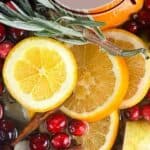 A photo of a blend of cranberries cinnamon sticks, fresh herbs, and oranges in water to make a christmas simmer pot set into a text box reading christmas simmer pot