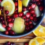 A photo of a blend of cranberries cinnamon sticks, fresh herbs, and oranges in water to make a christmas simmer pot set into a text box reading christmas simmer pot