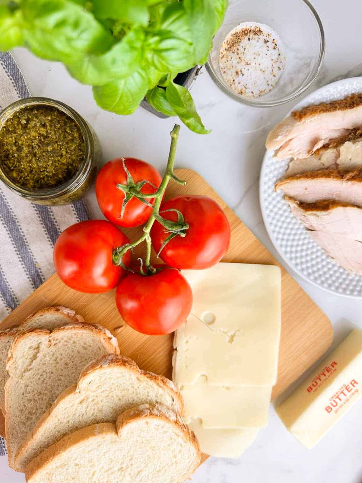 Ingredients for a turkey pesto panini: turkey, pesto, cheese, bread, butter, and tomatoes