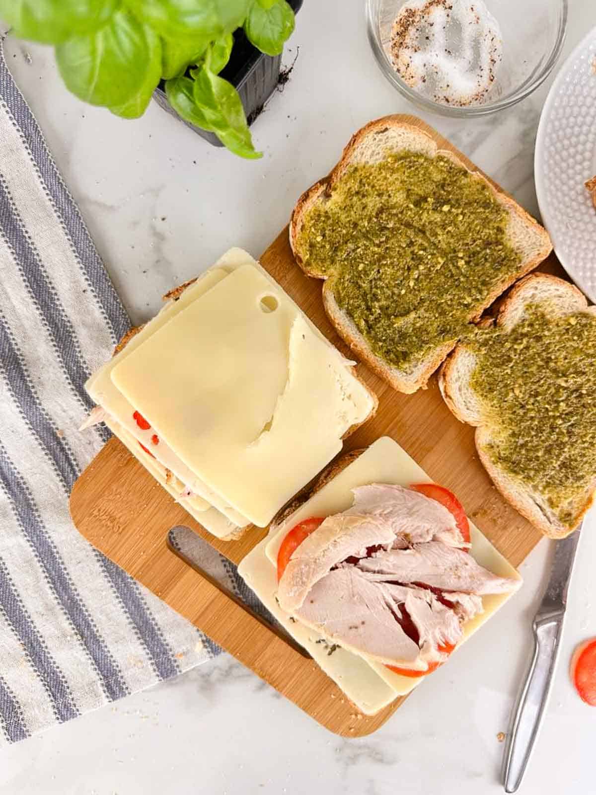 Build the turkey pesto panini by layering sliced cheese on to the pesto covered bread followed by turkey, tomato slices, and another slice of cheese.