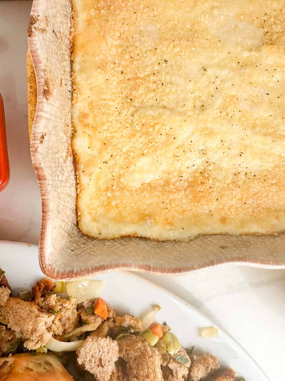 Twice baked potato casserole in a dish near a plate of stuffing