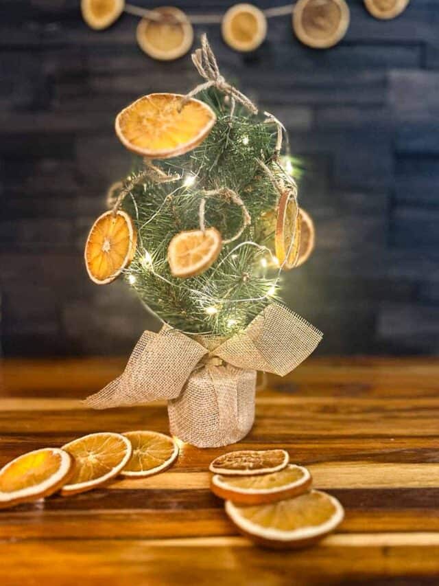 A mini Christmas tree decorated with dried orange slices on a kitchen counter with an orange slice garland hanging from the backsplash