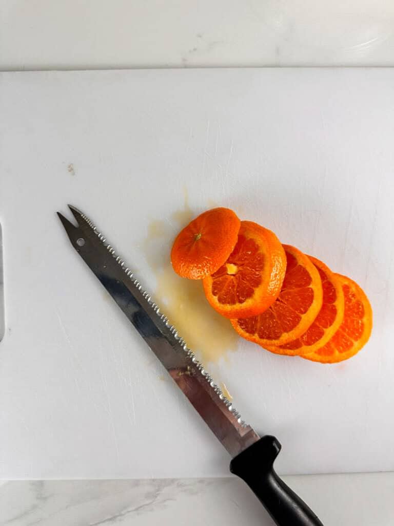 Sliced orange on a white cutting board with a serated knife.