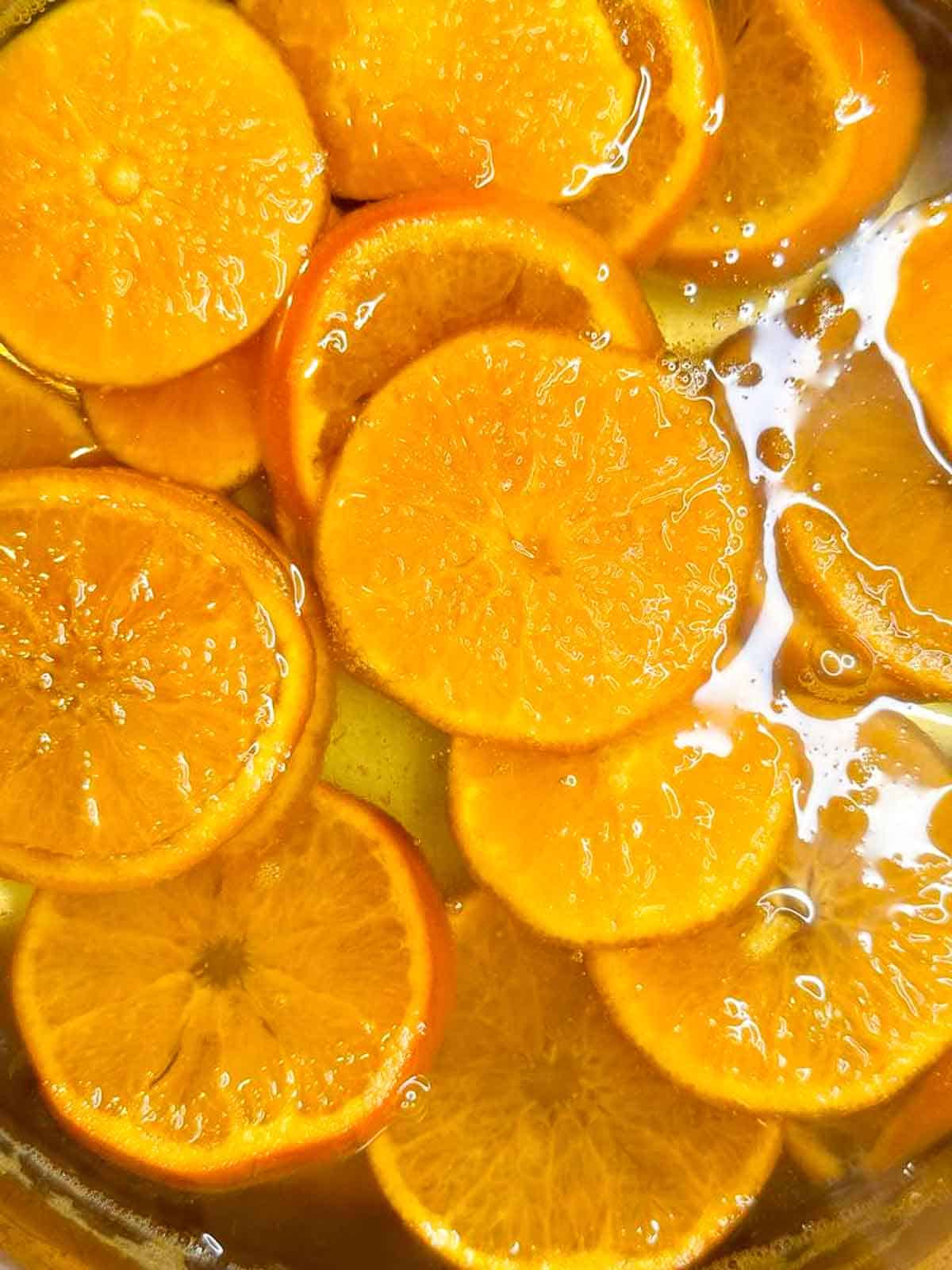 Orange slices in pot of simmering sugar water.