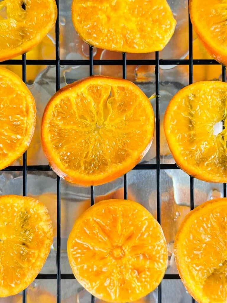 Boiled orange slices on a cooling rack sitting on a foil lined sheet.