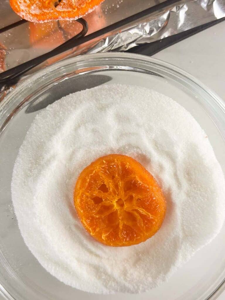 Candied orange slice dipped in bowl of granulated sugar.