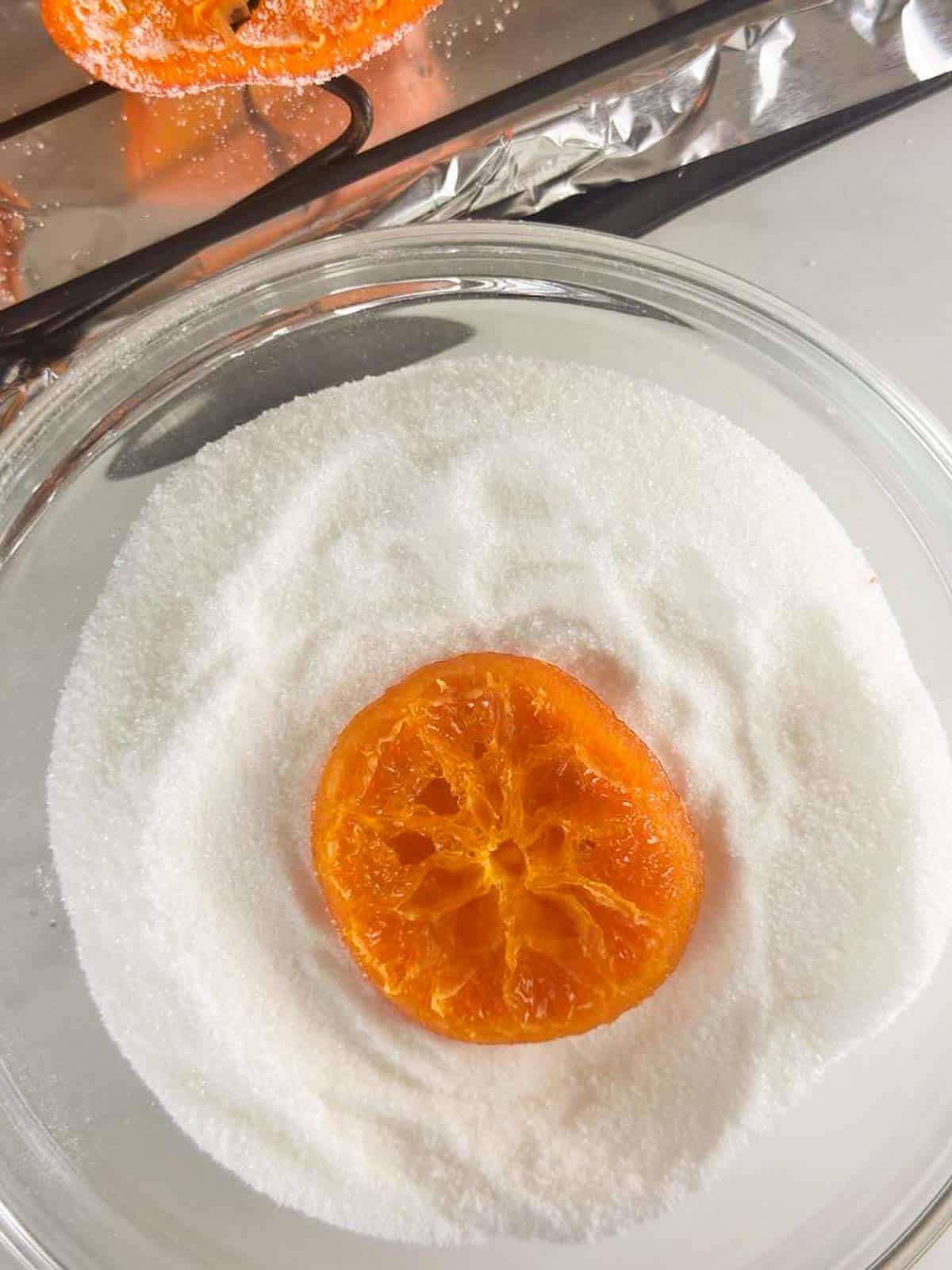 Candied orange slice dipped in bowl of granulated sugar.