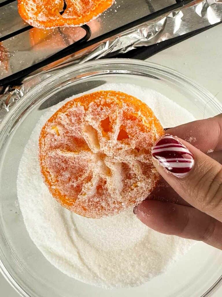 Candied orange slice coated in sugar held over a bowl of sugar.