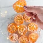 Picture of a hand holding a candied orange slice over plated orange slices with a caption that reads candied orange slices.