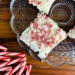 Plate of four candy cane brownies with some candy canes in the foregrounds and white twinkle lights on top of a butcher block counter.