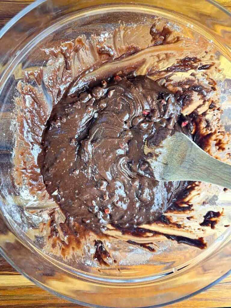 Mixing brownie mix with crushed candy canes or candy in a large, clear bowl using a wooden spoon.