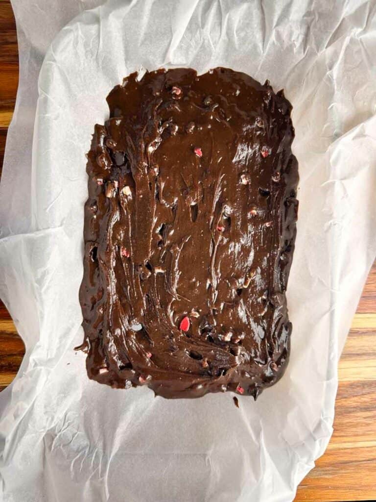 Brownie batter spread in a parchment paper lined rectangular baking pan.