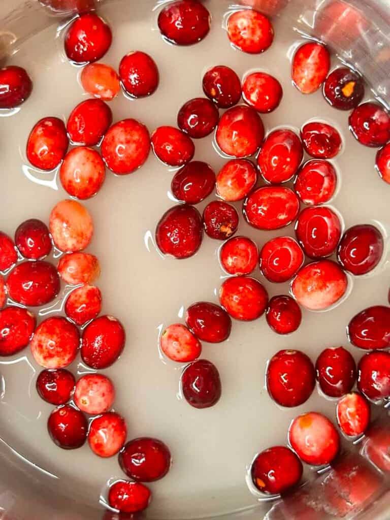 Fresh cranberries floating in pot with sugar and water.