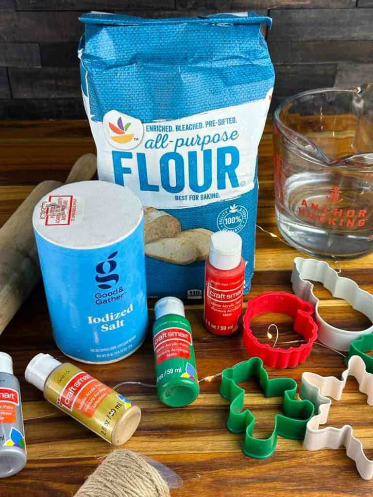 Supplies needed for salt dough ornaments: all purpose flour, salt, warm water, craft paint, twine, cookie cutters, and a rolling pin.