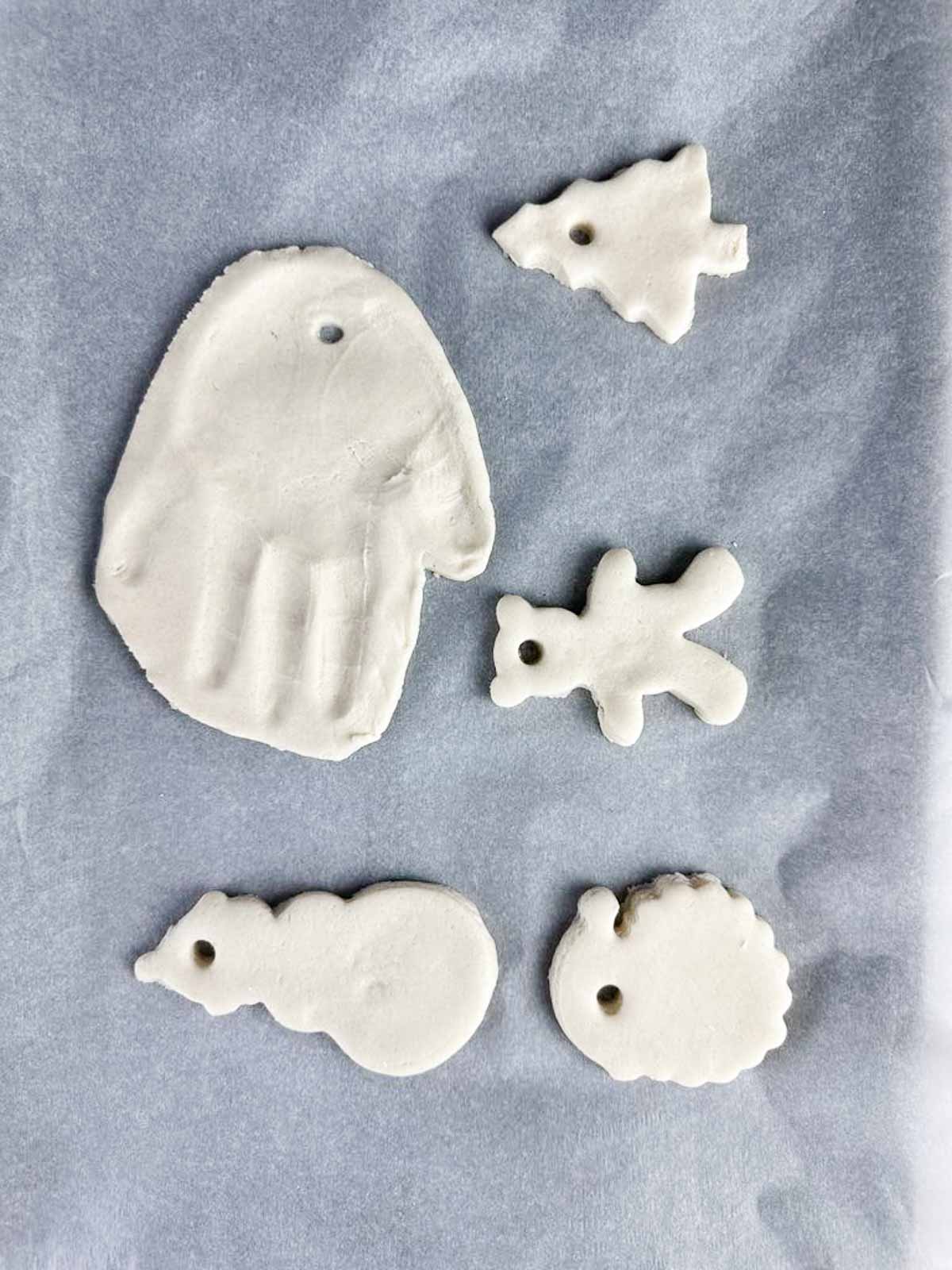 Sheet of salt dough Christmas ornaments ready to bake, including a handprint, teddy bear, Christmas tree, Santa, and a snowman.