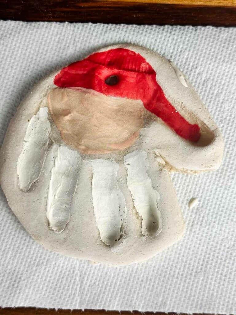 Baked salt dough ornament handprint with a painted on Santa hat, face, and beard in the finger prints.