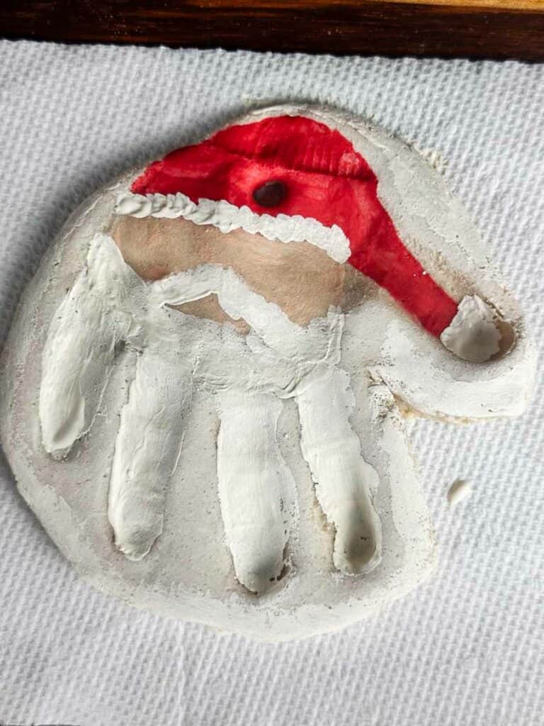 Salt dough ornament handprint with a painted on Santa hat, beard and mustache, and face.