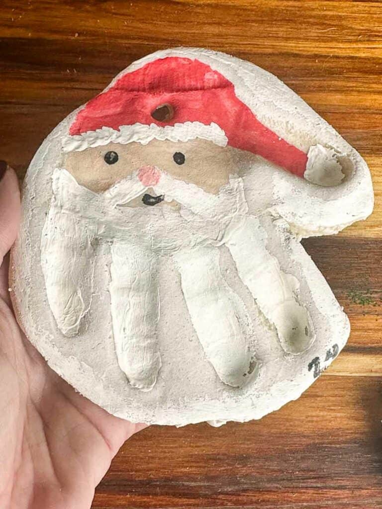 A finished salt dough ornament handprint with a Santa face and hand.