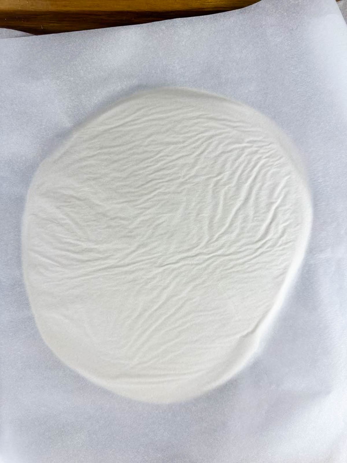 Picture of salt dough sandwiched between two sheets of parchment paper and flattened out to about 1/8 of an inch thickness.