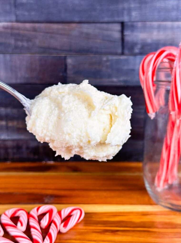 Scoop of peppermint frosting with candy canes in the background. Set in front of butcher block counter and wood back splash.