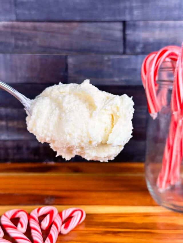 Scoop of peppermint frosting with candy canes in the background. Set in front of butcher block counter and wood back splash.