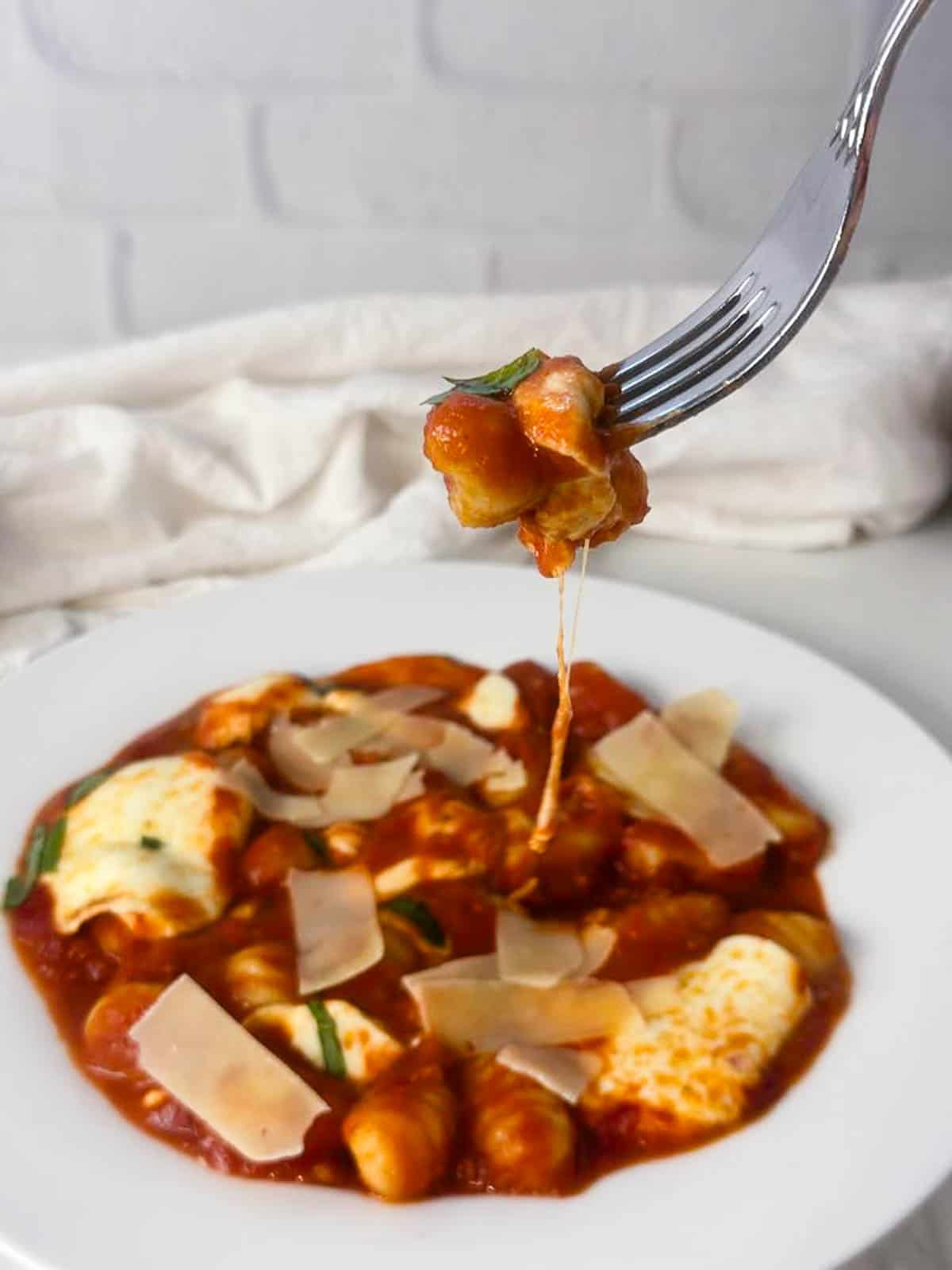 Taking a fork full of gnocchi alla Sorrentina out of a white bowl of gnocchi and sauce.