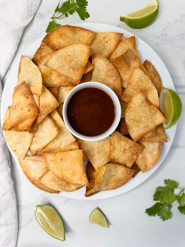 Plate of homemade corn tortilla chips with a dipping sauce and lime wedges.